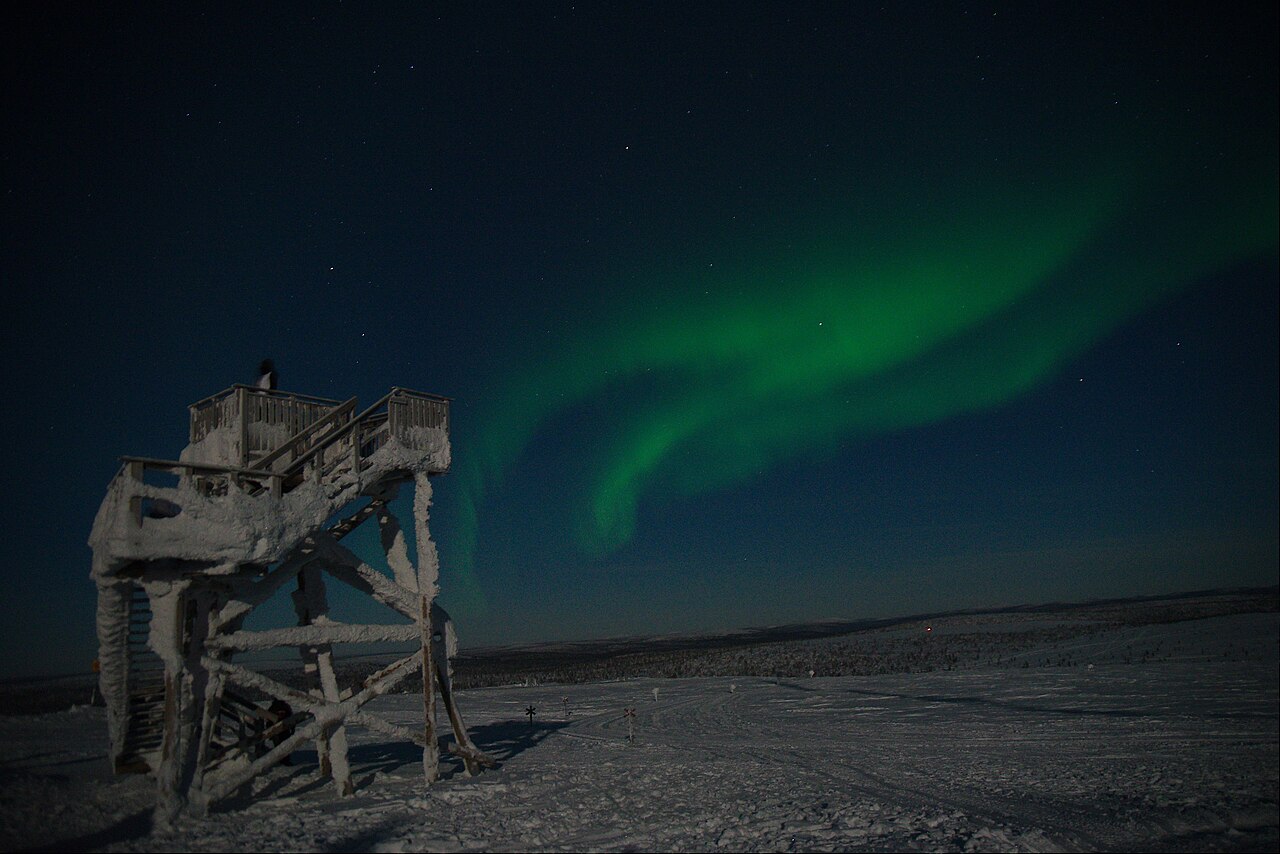 Green northern lights above a snow-covered lookout and fell landscape in Saariselkä.